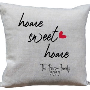 May include: A white throw pillow with the text "home sweet home" in black cursive font. A small red heart is next to the word "sweet". The text "The Pearson Family 2020" is printed below in black cursive font.