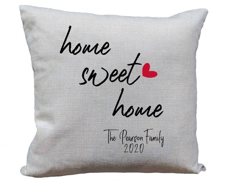 May include: A white throw pillow with the text "home sweet home" in black cursive font. A small red heart is next to the word "sweet". The text "The Pearson Family 2020" is printed below in black cursive font.