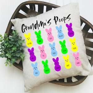 May include: A white cushion with the text "Grandma's Peeps" in black. The cushion is decorated with 16 colourful, cartoon-style peeps, each with a different name written underneath.