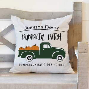 May include: White throw pillow with a green truck carrying pumpkins. The text on the pillow reads "Johnson Family Pumpkin Patch Pumpkins Hay Rides Cider".