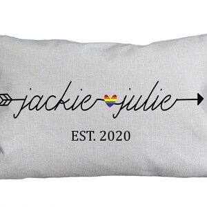 May include: A white pillow with a black arrow and the text "jackie julie" with a rainbow heart in between the names. The text "EST. 2020" is below the names.