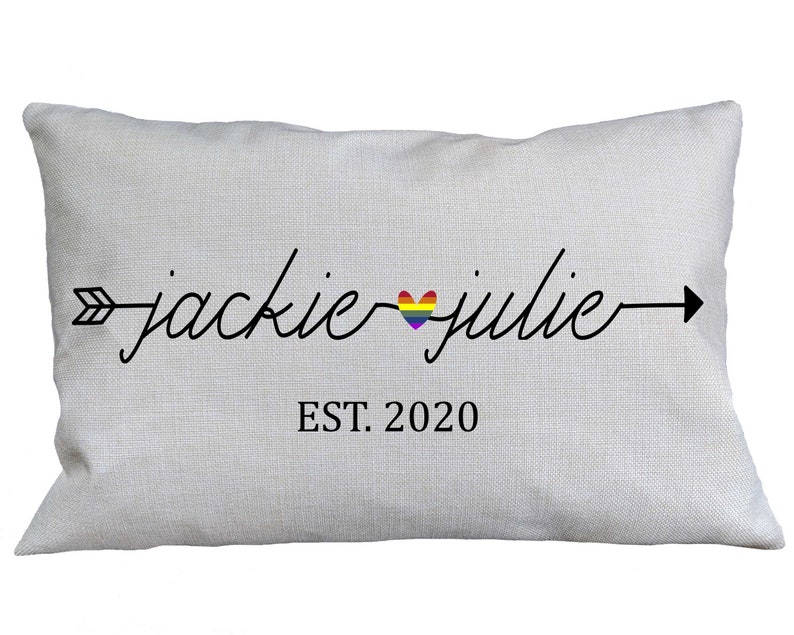 May include: A white pillow with a black arrow and the text "jackie julie" with a rainbow heart in between the names. The text "EST. 2020" is below the names.