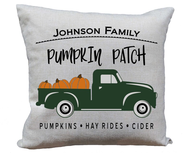 May include: A white pillow with the text "JOHNSON FAMILY PUMPKIN PATCH PUMPKINS HAY RIDES CIDER" and a green truck with three orange pumpkins in the bed.