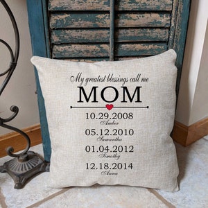 Może przedstawiać: Beżowa poduszka z napisem "My greatest blessings call me MOM" i czerwonym sercem. Pod tekstem znajdują się daty i imiona czworga dzieci: 10.29.2008 Amber, 05.12.2010 Samantha, 01.04.2012 Timothy, 12.18.2014 Anna.