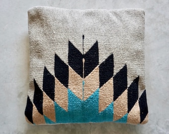 May include: A gray throw pillow with a geometric pattern in black, beige, and teal. The pattern is a series of triangles that form a diamond shape in the center.