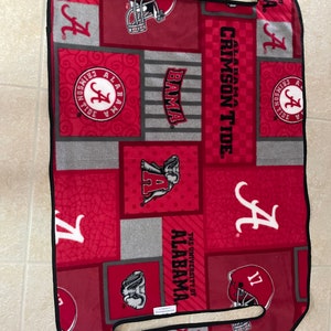 May include: A red, gray, and white fleece blanket with the University of Alabama logo and the words "Crimson Tide" and "Bama".