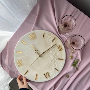 Person carefully adjusting the clock, displaying the resin finish and elegant gold accents.