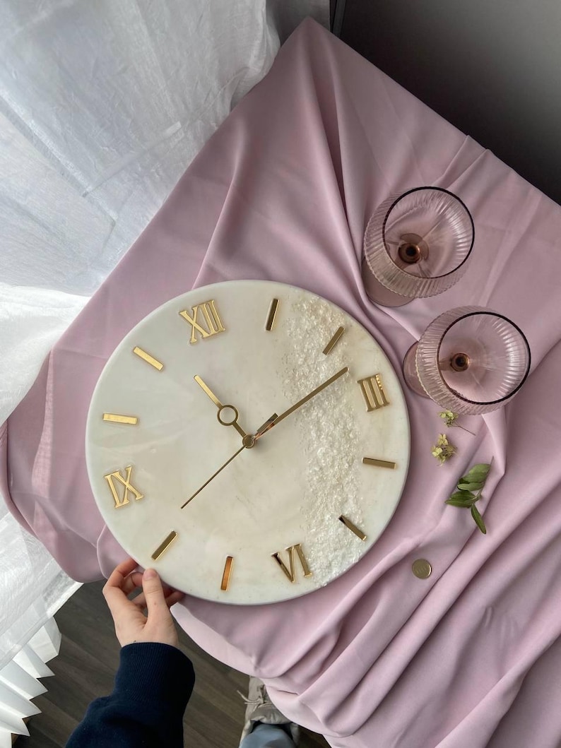 Person carefully adjusting the clock, displaying the resin finish and elegant gold accents.