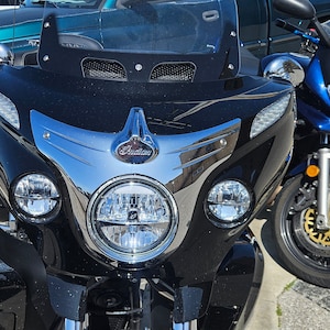 May include: A black motorcycle with chrome accents and a large windscreen. The motorcycle has two headlights and a chrome Indian logo on the front.