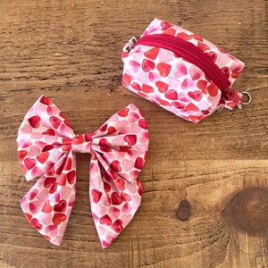 May include: A pink and red bow with a heart pattern. The bow is made of fabric and has a large, flat center. The bow is tied with a knot in the center.