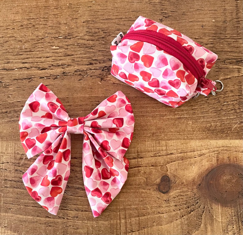 May include: A pink and red bow with a heart pattern. The bow is made of fabric and has a large, flat center. The bow is tied with a knot in the center.