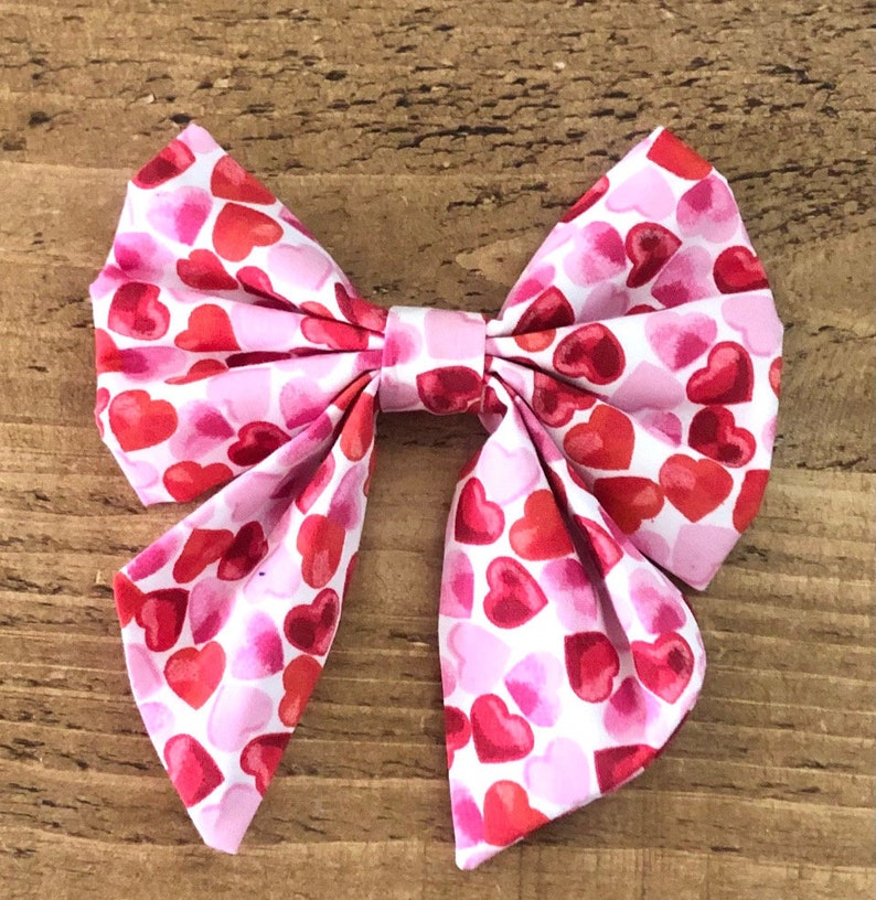 May include: A pink and red bow with a heart pattern. The bow is made of fabric and is tied in a knot.