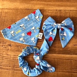 May include: A set of three blue and white fabric accessories featuring a cartoon dog with the words "Smile", "Giggle", and "Laugh". The set includes a bandana, a hair bow, and a scrunchie.