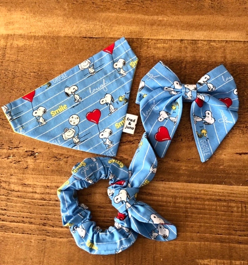 May include: A set of three blue and white fabric accessories featuring a cartoon dog with the words "Smile", "Giggle", and "Laugh". The set includes a bandana, a hair bow, and a scrunchie.