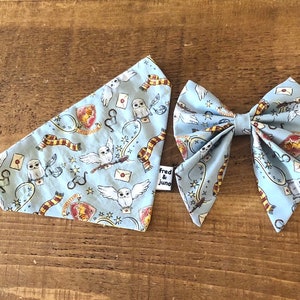 May include: A light blue bandana and bow tie set with a Harry Potter themed print featuring owls, wands, and the Hogwarts crest. The bandana has a Fred & Juno label.