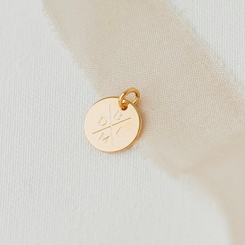 May include: A gold-colored charm with the letters D, B, L, and M engraved in a cross pattern.