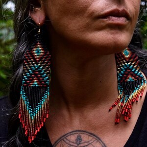 May include: Handmade beaded earrings with a geometric design. The earrings feature a black base with turquoise, red, and gold accents. The fringe earrings are long and dangle, adding movement and flair. These earrings are a unique accessory.