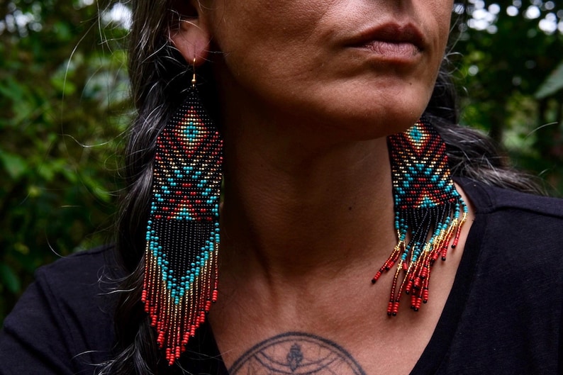May include: Handmade beaded earrings with a geometric design. The earrings feature a black base with turquoise, red, and gold accents. The fringe earrings are long and dangle, adding movement and flair. These earrings are a unique accessory.