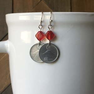 May include: Silver earrings with red glass beads and Japanese coins featuring Mount Fuji. The coins have Japanese characters on them.