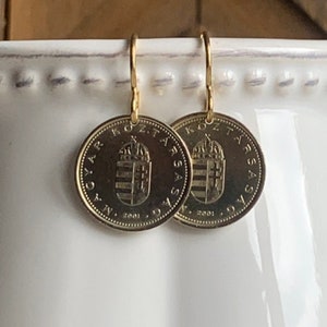 May include: Gold dangle earrings featuring a Hungarian 1 Forint coin from 2001. The coin features the Hungarian coat of arms with a crown and the text "MAGYAR KOZTARSASAG" around the edge.