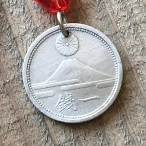 May include: A silver coin with a depiction of Mount Fuji and a rising sun. The coin has a raised rim and the Japanese word "銭" (sen) is inscribed on the bottom.