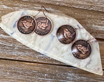 May include: Two pairs of copper-toned coin earrings featuring a wren bird design. One pair is dated 1950 and the other pair is dated 1940. Each coin is inscribed with the word FARTHING and is attached to a curved metal ear wire for hanging.