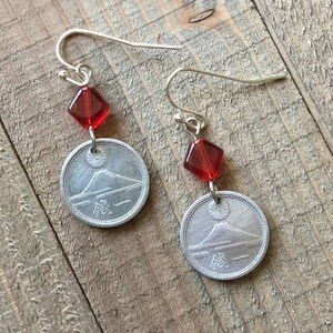 May include: Silver earrings with red glass beads and Japanese coins featuring Mount Fuji. The coins have Japanese characters and a sun design.
