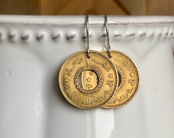 May include: Gold coin earrings with Arabic script and a star design. The coins are from 1966 and feature a wreath around the star.
