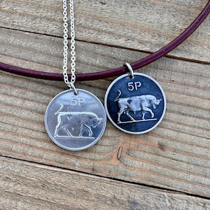 Puede incluir: Dos collares de plata con un colgante de moneda de 5 peniques con un diseño de toro. Un collar tiene un cordón de cuero marrón y el otro una cadena de plata.