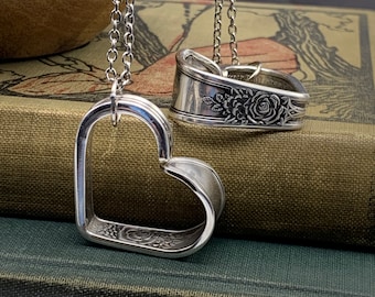 May include: Two silver heart-shaped pendants with floral designs hanging on chains. The pendants are made from repurposed silverware.