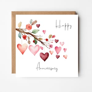 Op de afbeelding: Een witte kaart met de woorden "Happy Anniversary" in zwarte cursieve letters. Een aquarel-illustratie van een tak met roze en rode bloemen en harten die eraan hangen.