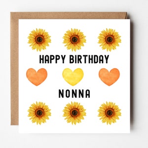 Op de afbeelding: Een witte kaart met de tekst "Happy Birthday Nonna" in het zwart. De kaart is versierd met zes gele zonnebloemen en drie harten, twee oranje en één gele.