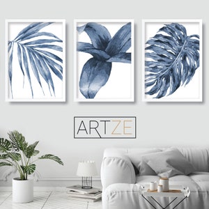 Puede incluir: Tres impresiones de acuarela de hojas tropicales azules enmarcadas. Las impresiones est&aacute;n en marcos blancos y est&aacute;n dispuestas en una fila en una pared blanca.