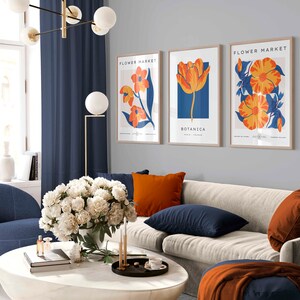May include: Three framed art prints with a floral theme. The prints feature orange and yellow flowers on a blue background. The text on the prints reads "Flower Market" and "Botanica".