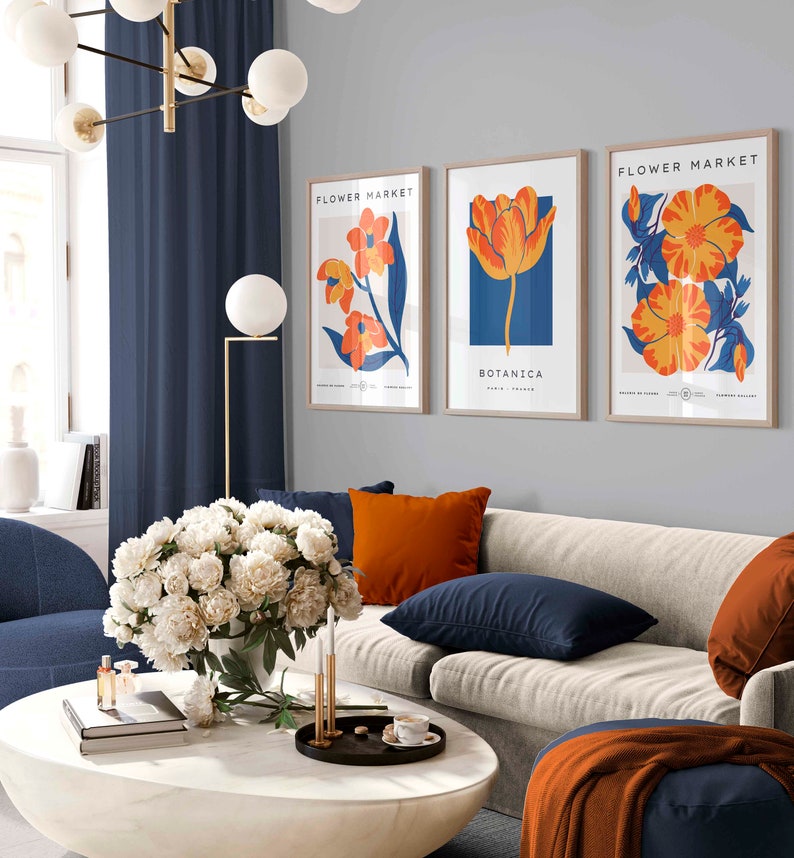 May include: Three framed art prints with a floral theme. The prints feature orange and yellow flowers on a blue background. The text on the prints reads "Flower Market" and "Botanica".