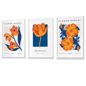 May include: Three framed prints with a white background and blue and orange floral designs. The top of each print reads "FLOWER MARKET" and the bottom reads "GALLERY OF FLOWERS". The middle print also has the text "BOTANICA PARIS - FRANCE".
