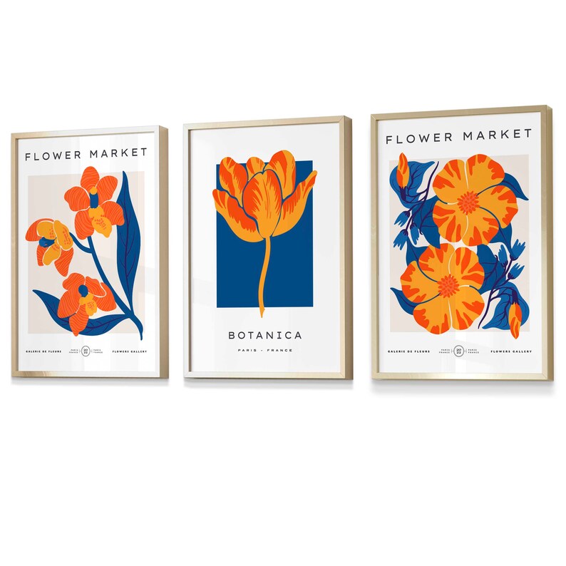 May include: Three framed prints with floral designs. The first print features a single orange and yellow tulip on a blue background with the text "BOTANICA PARIS - FRANCE". The second print features a branch of orange and yellow flowers with blue leaves on a cream background with the text "FLOWER MARKET". The third print features two orange and yellow flowers with blue leaves on a cream background with the text "FLOWER MARKET".