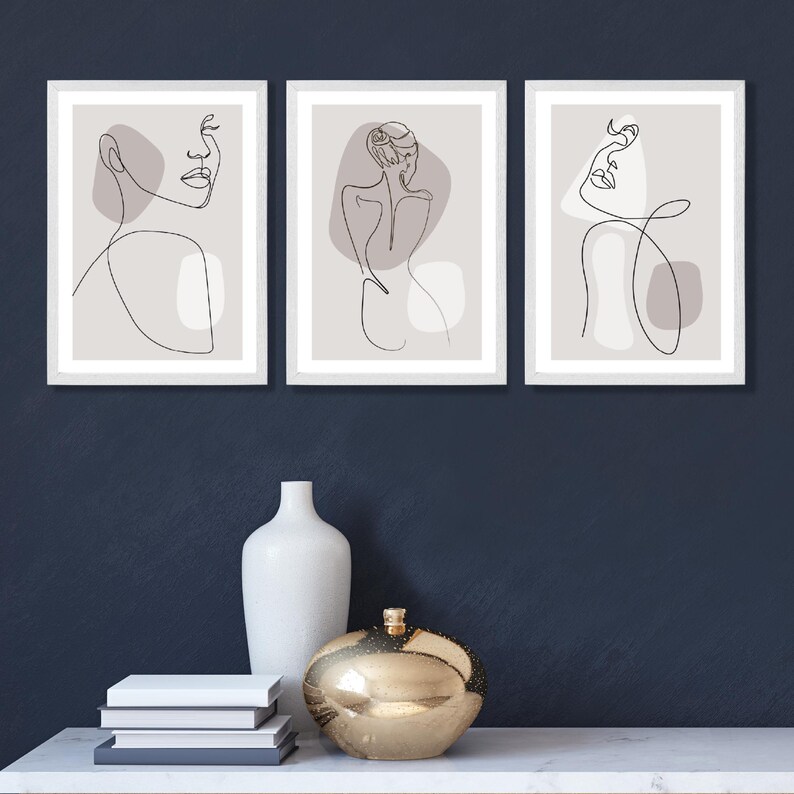 May include: Three framed minimalist line art prints with a grey background. Each print features a single line drawing of a woman's face and body.