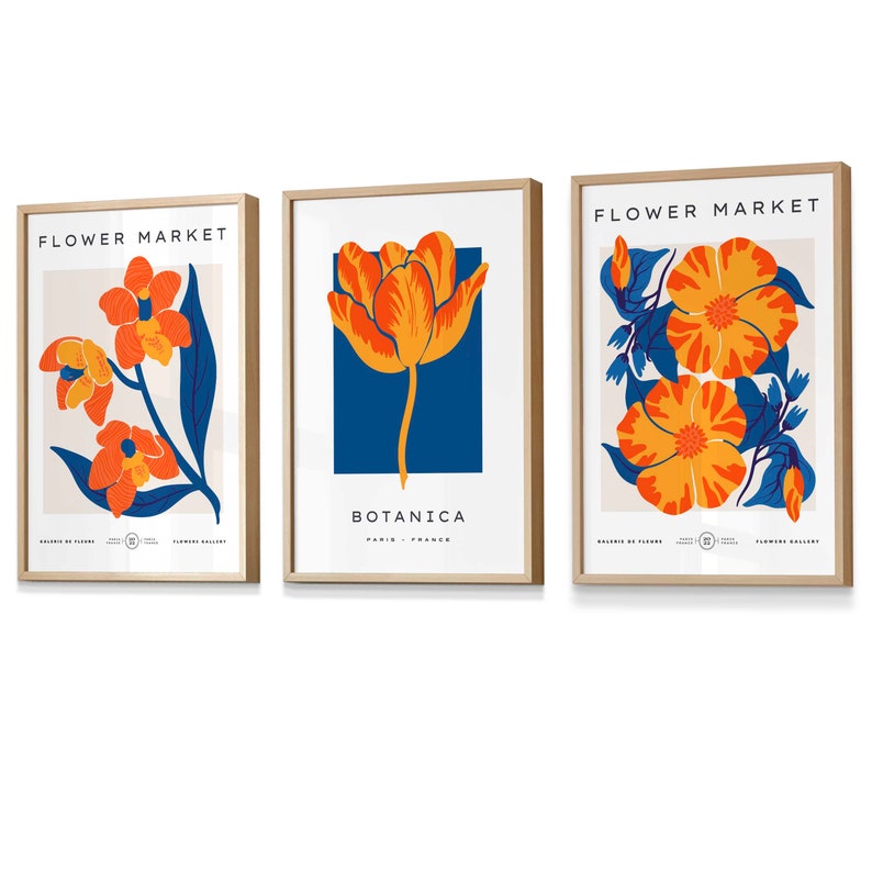 May include: Three framed prints with a floral theme. The prints feature a single orange tulip, a cluster of orange flowers, and a single orange flower with blue leaves. Each print has the text "FLOWER MARKET" at the top and "BOTANICA" at the bottom.