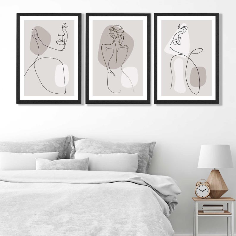 May include: Three minimalist line art prints in black frames on a white wall. Each print features a single line drawing of a woman's face or body with abstract shapes in shades of grey.
