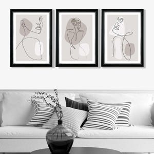 May include: Set of three black framed prints with minimalist line drawings of female figures on a light grey background. Each print features a different pose and abstract shapes.