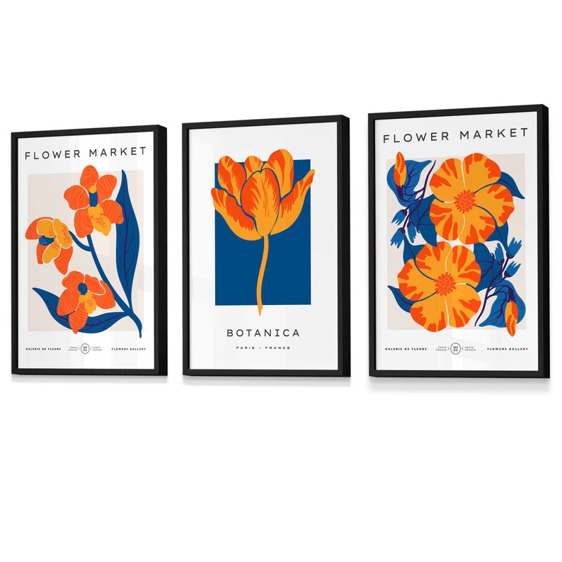 May include: Three black framed prints with floral illustrations. The first print features orange and yellow flowers with blue leaves on a cream background. The second print features a single orange and yellow tulip on a blue background. The third print features orange and yellow flowers with blue leaves on a cream background. All prints have the text "FLOWER MARKET" at the top and "BOTANICA" at the bottom.