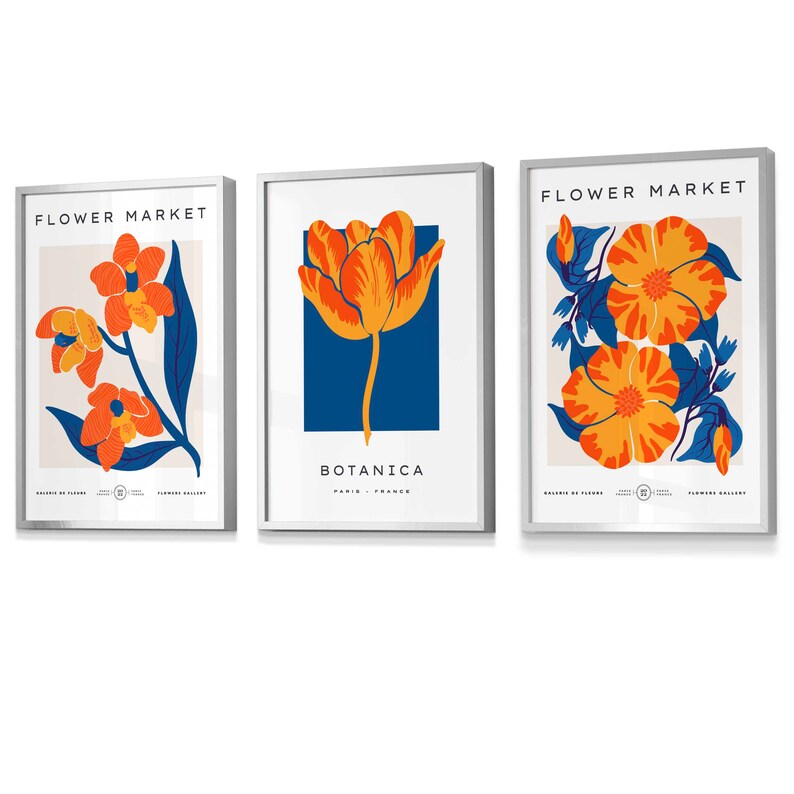 May include: Three framed prints with floral designs. The first print features orange and yellow flowers with blue leaves on a light pink background. The second print features a single orange and yellow tulip on a blue background. The third print features orange and yellow flowers with blue leaves on a light pink background. All three prints have the text "FLOWER MARKET" at the top and "BOTANICA" at the bottom.