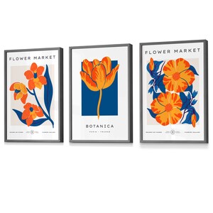 May include: Three framed prints with a floral theme. The prints feature orange and yellow flowers with blue and white backgrounds. The text on the prints reads "Flower Market" and "Botanica Paris, France".