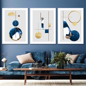 May include: Three framed abstract art prints with geometric shapes in shades of blue and gold on a gray background. The prints are hung on a blue wall.
