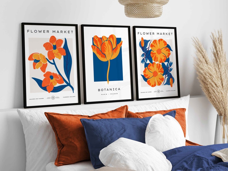 May include: Three framed prints with black frames and white backgrounds. Each print features a different stylized flower in orange and yellow with blue accents. The prints are titled "Flower Market" and "Botanica".