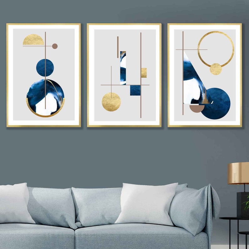 May include: Three abstract art prints with gold and blue geometric shapes on a white background. The prints are framed in gold and hung on a blue wall.
