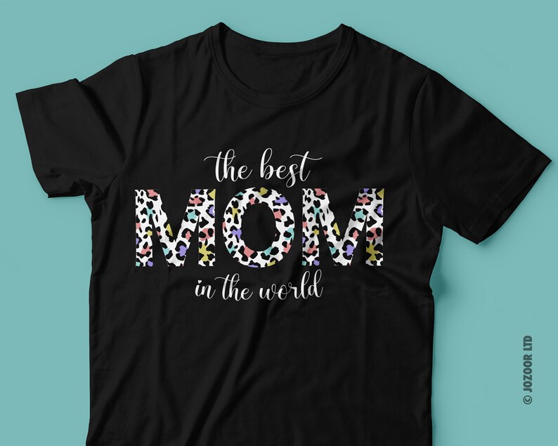 Puede incluir: Camiseta negra con el texto "the best MOM in the world" en letras blancas. La palabra "MOM" est&aacute; en un estampado de leopardo colorido.