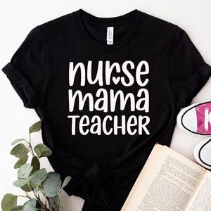 May include: Black t-shirt with the words "nurse mama teacher" in white, with a heart replacing the letter "o" in "nurse". The shirt is paired with pink sneakers and an open book.