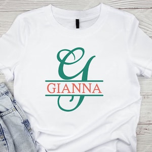 May include: White t-shirt with a teal green cursive letter "G" and the name "GIANNA" in coral red lettering.
